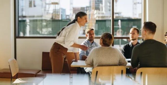 Woman leading a meeting in a bright office with five people seated around a table.