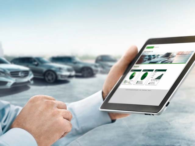 Person holding a tablet displaying graphs and a webpage, with several cars blurred in the background.