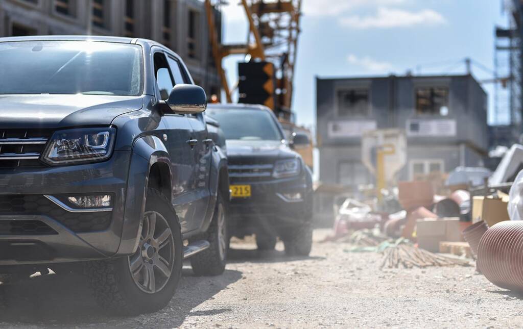Cars parked at a dusty construction site with machinery and building materials in the background.