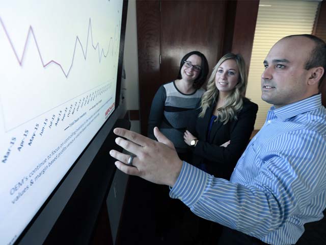 Three people discussing a line graph on a large screen in an office setting.