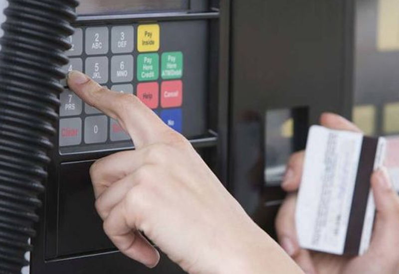 Person entering a PIN at a gas pump keypad while holding a card in the other hand.