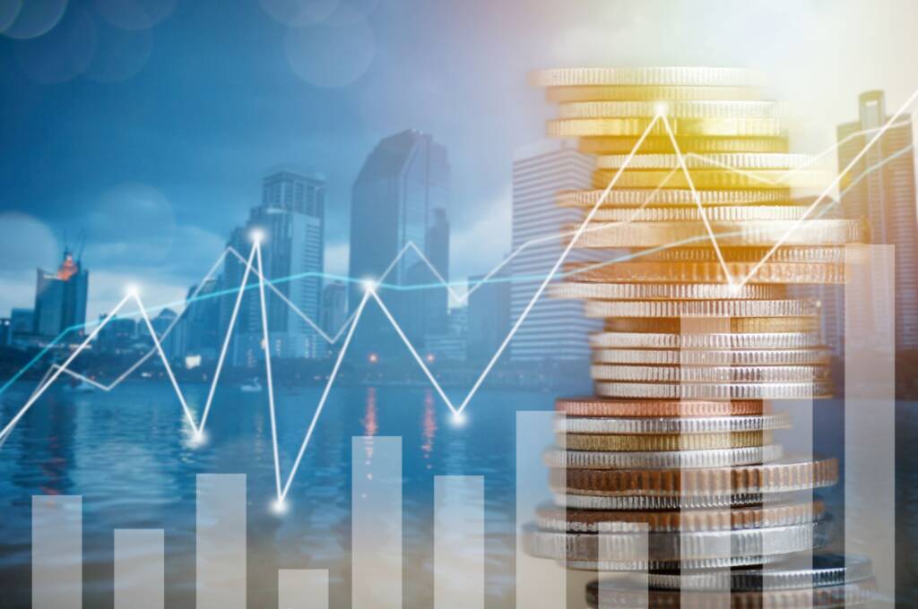 Stacks of coins with a city skyline in the background, overlaid with upward trending financial graphs.