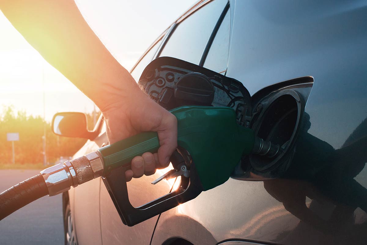 Person refueling a car with a green gas pump nozzle against a sunset background.