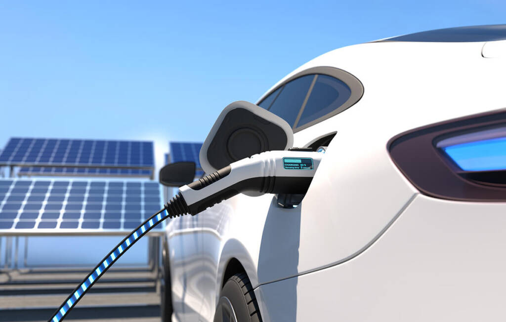 Electric car charging at a station, with solar panels in the background under a clear blue sky.