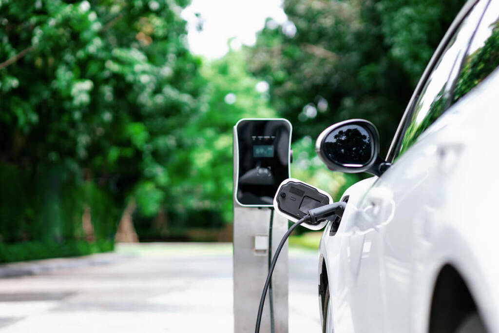 Electric car charging at a station, surrounded by green trees.