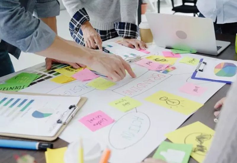 People collaborating on a table with sticky notes, a laptop, coffee cups, and charts.