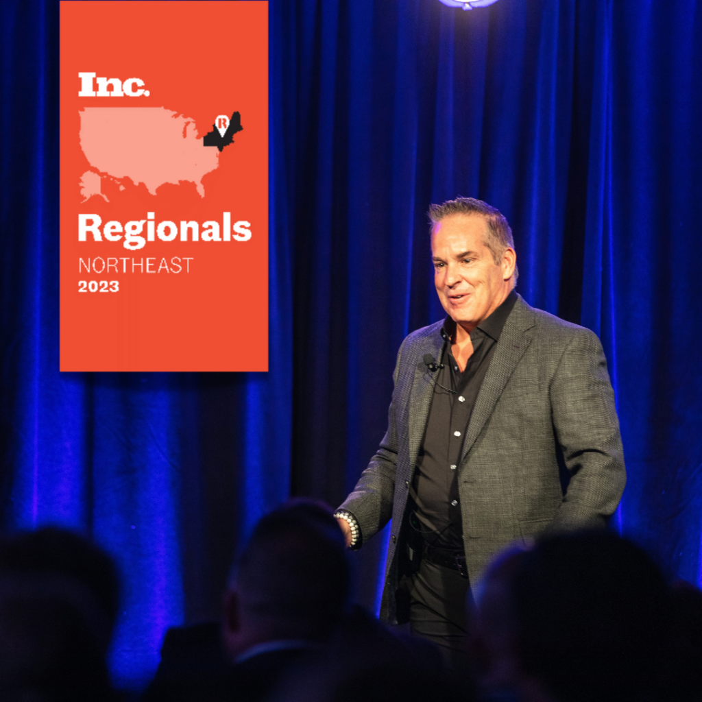 Speaker in a grey suit on stage at Inc. Regionals Northeast 2023 event with a red banner on the side.