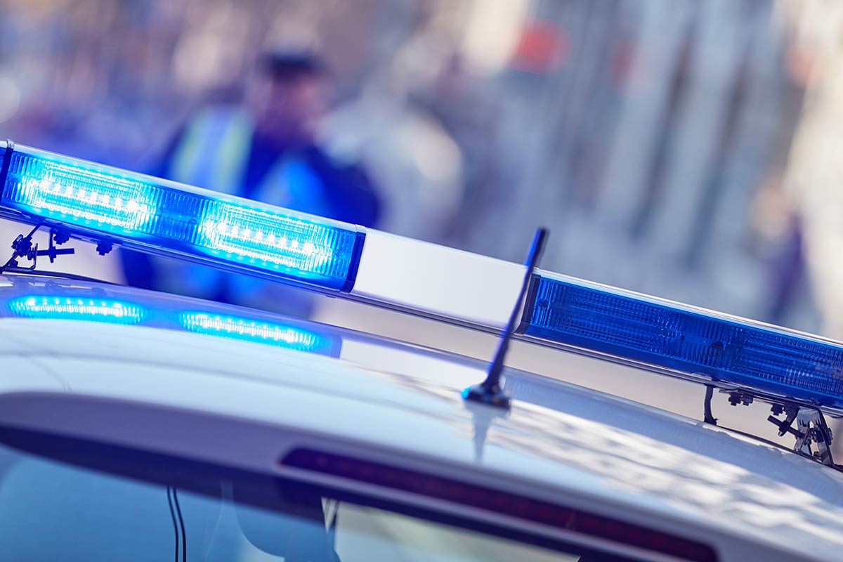 Close-up of a police car's roof with flashing blue lights, blurred figure in the background.