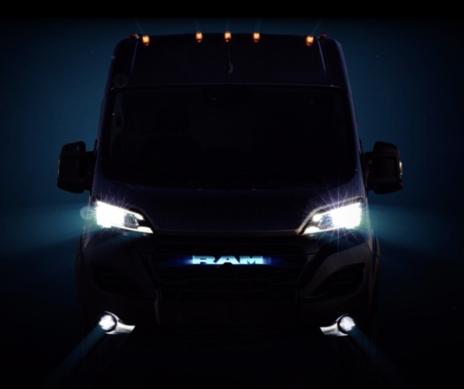 Front view of a RAM truck at night with illuminated headlights and logo, surrounded by darkness.
