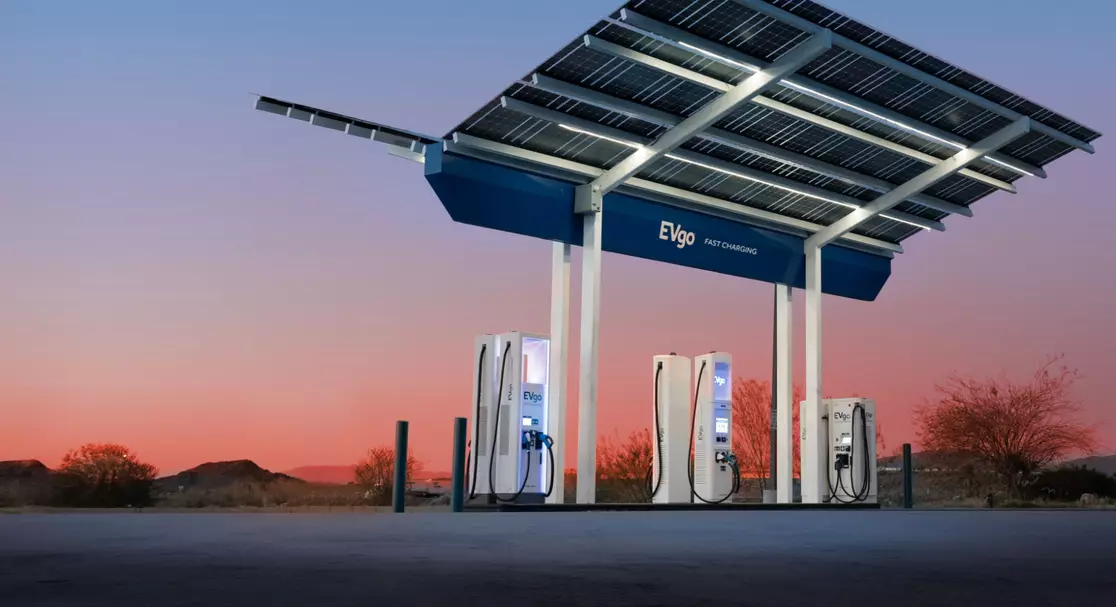 EV charging station with solar panels at sunset, featuring three chargers in a desert landscape.