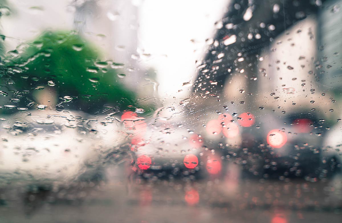 Blurry cityscape viewed through a rain-splattered window, with traffic lights glowing in the background.