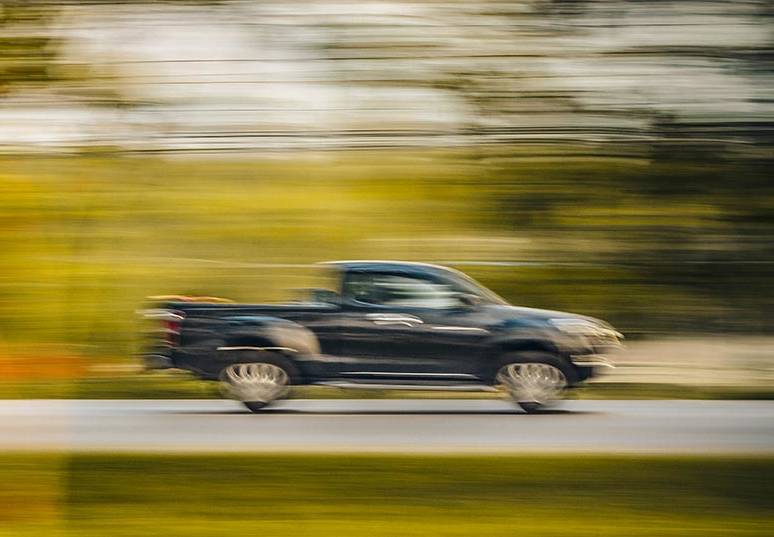 A black pickup truck in motion, creating a blurred effect against a green landscape background.