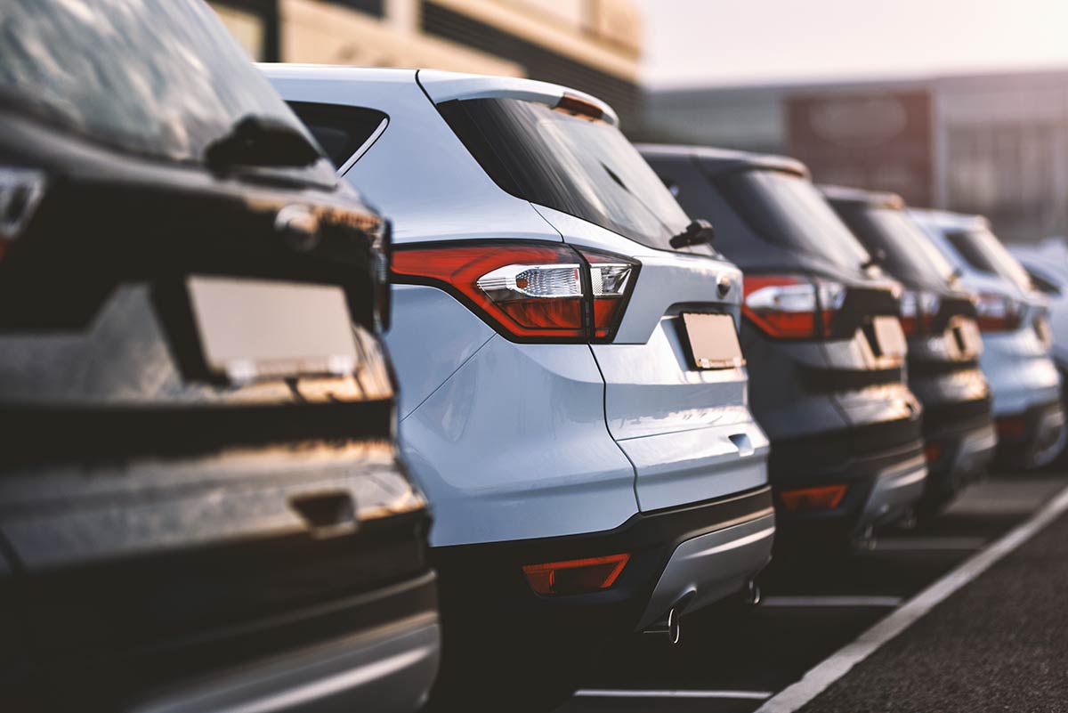 A row of parked cars with focus on a white SUV, viewed from behind in a parking lot at sunset.
