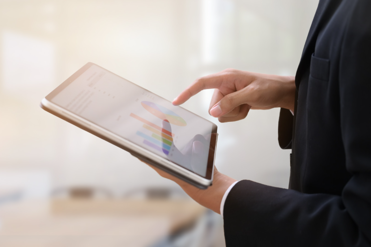 Person in suit using a tablet displaying colorful charts in a bright office environment.