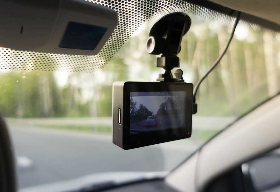 Dashcam mounted on a car windshield, recording the road with trees in the background.