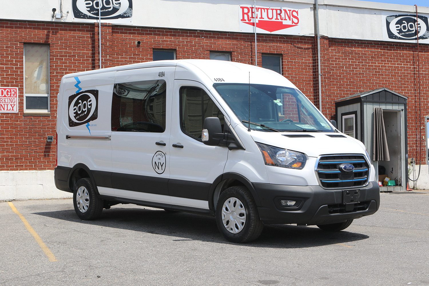 White delivery van parked outside a brick building with signs for "edge" and "RETURNS".