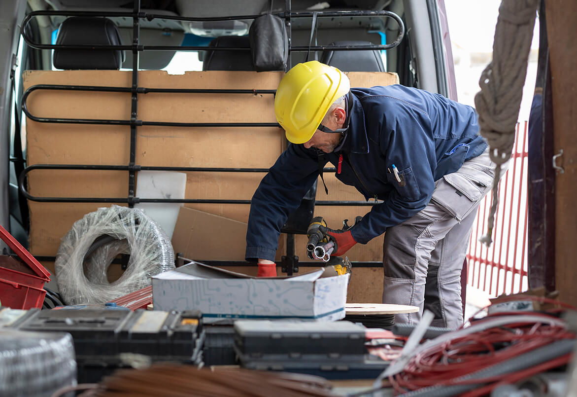 Worker in a hard hat organizing supplies in the back of a van, surrounded by tools and equipment.