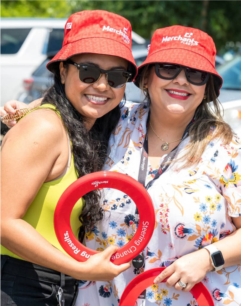 Two women smiling, wearing red hats and holding red frisbees, outdoors.