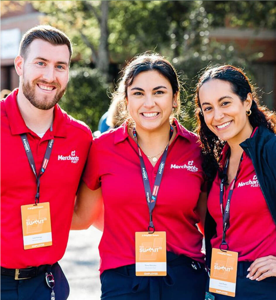 Three people in red shirts with name tags smiling outdoors.