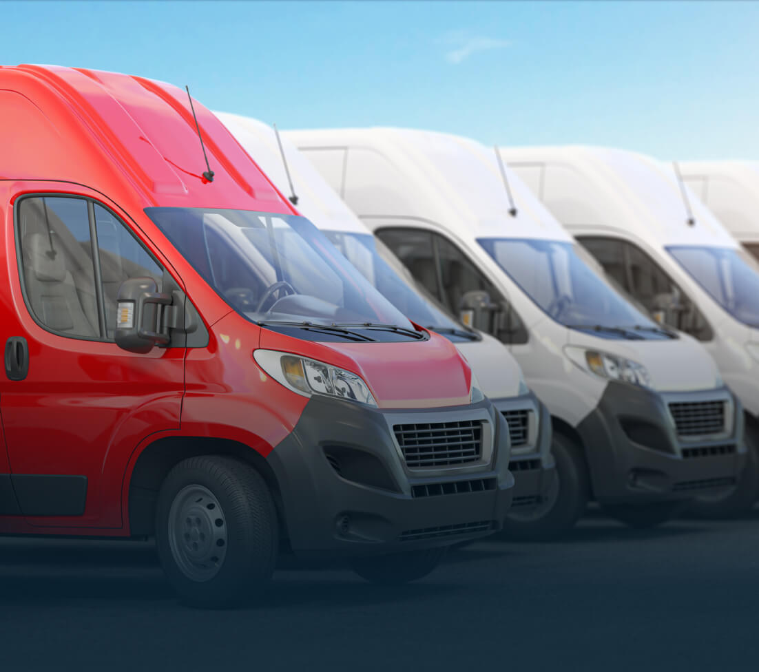 A row of parked vans, with one red van in front and several white vans behind, under a clear blue sky.