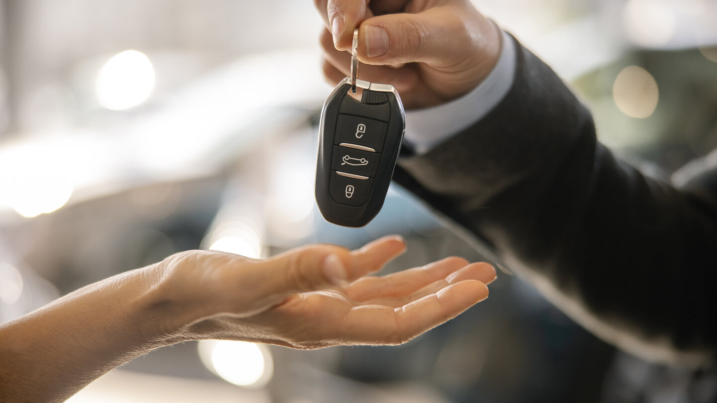 A hand gives a car key to another hand, palm up, in a close-up shot with a blurred background.