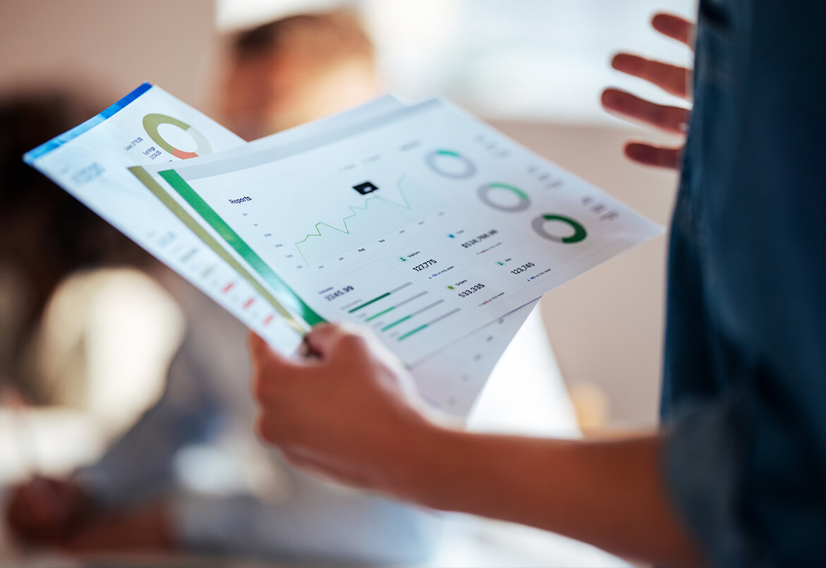 Person holding business charts with graphs and data, gesturing in a meeting.