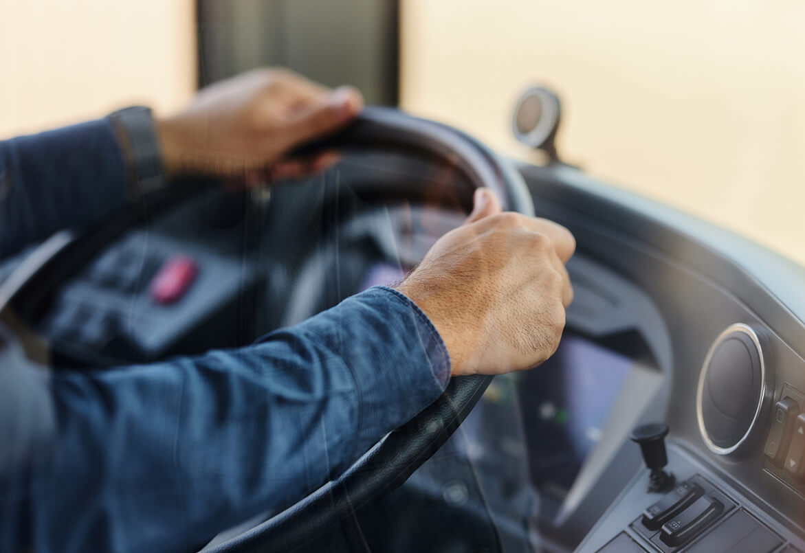 Close-up of a person in a blue shirt holding a steering wheel in a vehicle interior.