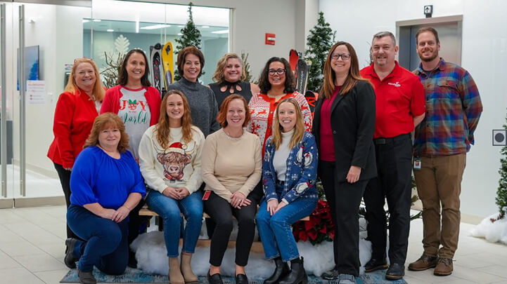 Group of people posing indoors in festive attire, with winter decorations and trees in the background.