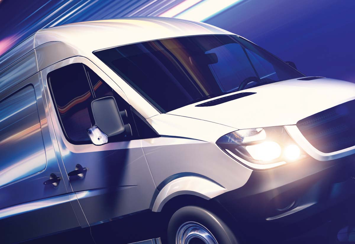 A white van speeds through a blurred cityscape, headlights on and windows reflecting light.