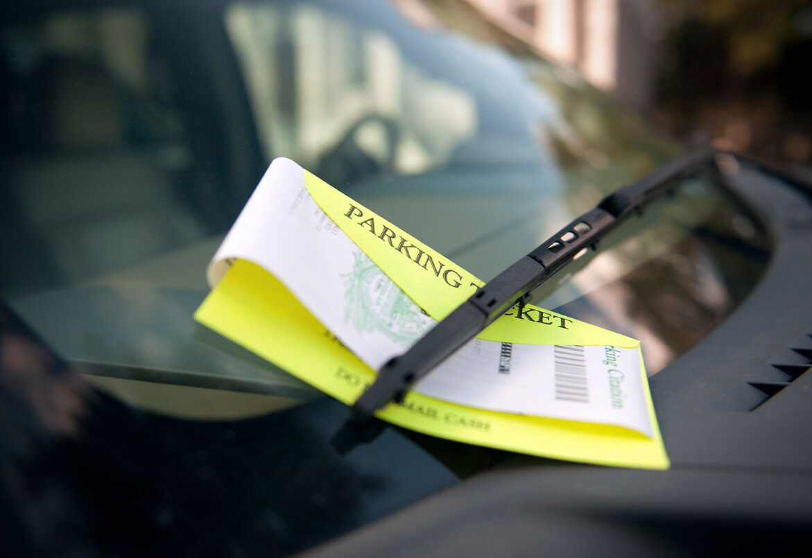 Parking ticket tucked under a windshield wiper on a car's front windshield.