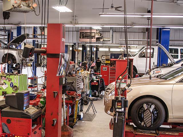 Busy auto repair shop with cars on lifts and various tools and equipment around.