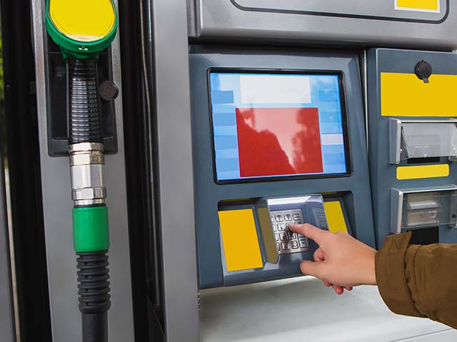 Hand entering PIN on a keypad at a gas pump with a green fuel nozzle.