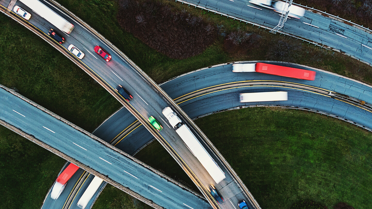 Aerial view of vehicles on a curving highway interchange with green grass surrounding.