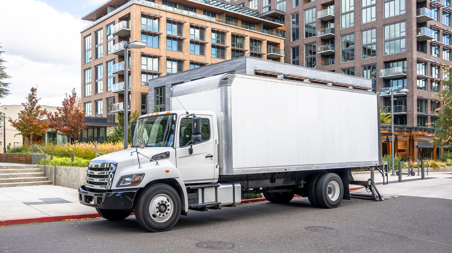 White delivery truck parked on a city street in front of modern apartment buildings.