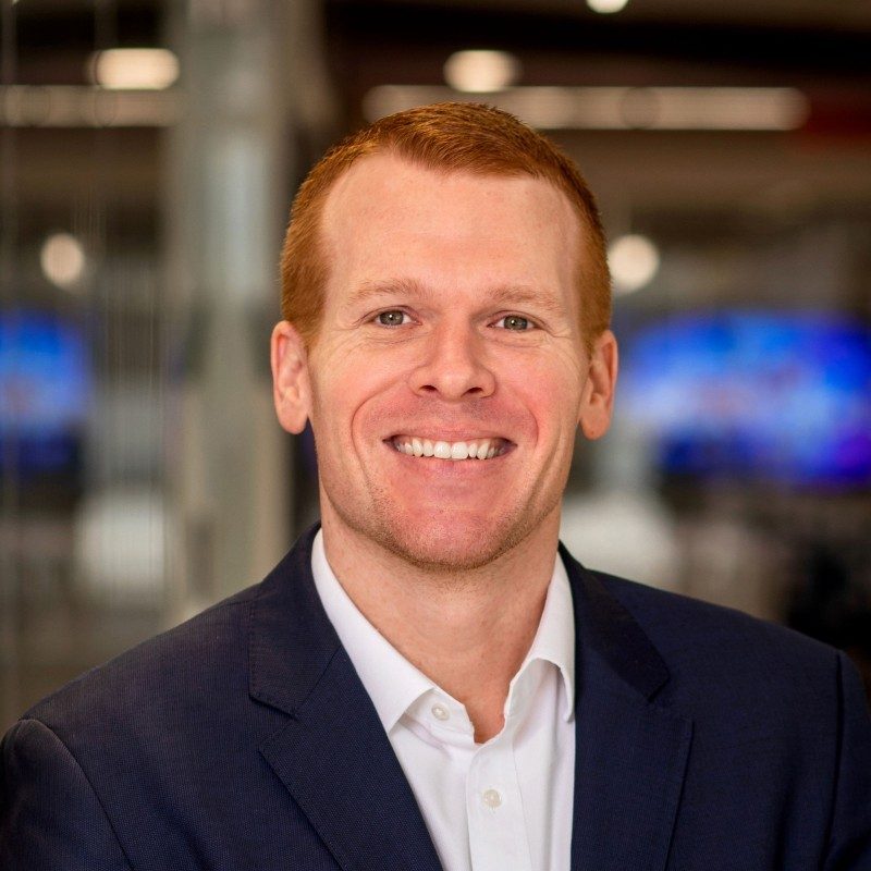 Smiling man in a suit with a blurred office background.