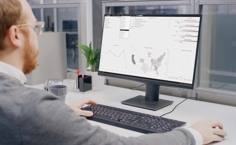 Person analyzing graphs and maps on a computer screen at an office desk.