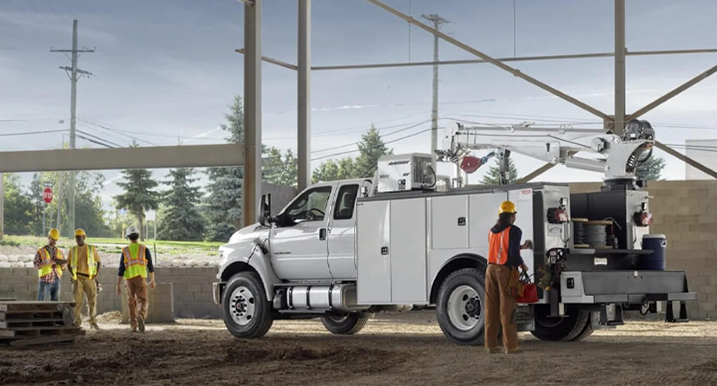 Construction workers and a white utility truck at a building site with metal beams and a brick wall.