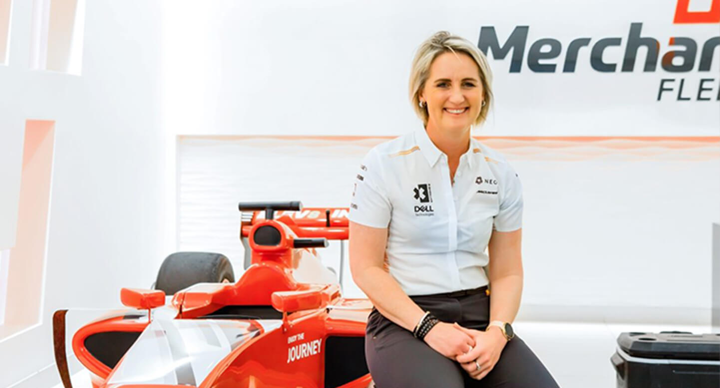Person sitting on a red race car in a bright showroom, smiling at the camera.