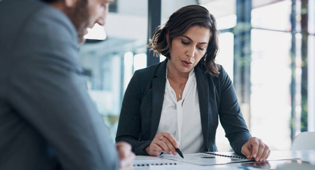 Two professionals reviewing documents at a table in a modern office setting.
