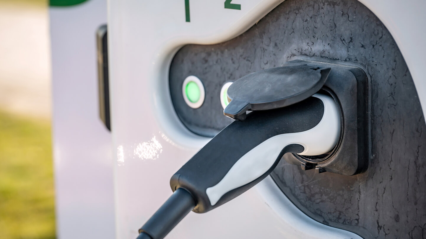 Close-up of an electric vehicle charging plug connected to a charging station with green indicator lights.