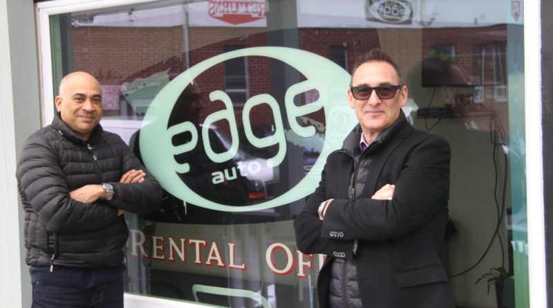 Two men in jackets stand with arms crossed outside the Edge Auto rental office.