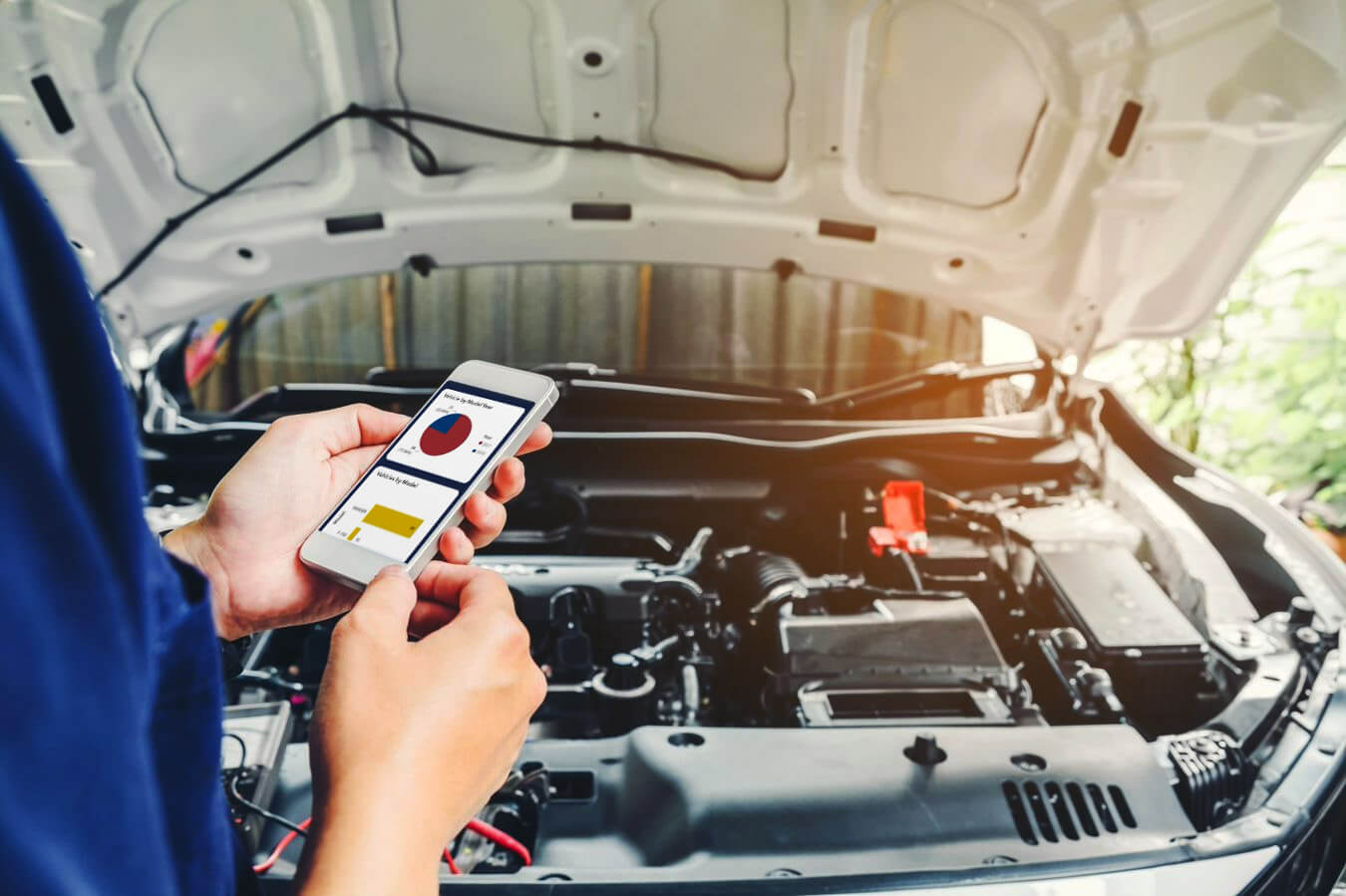 Person using a smartphone to check car diagnostics in front of an open car hood.