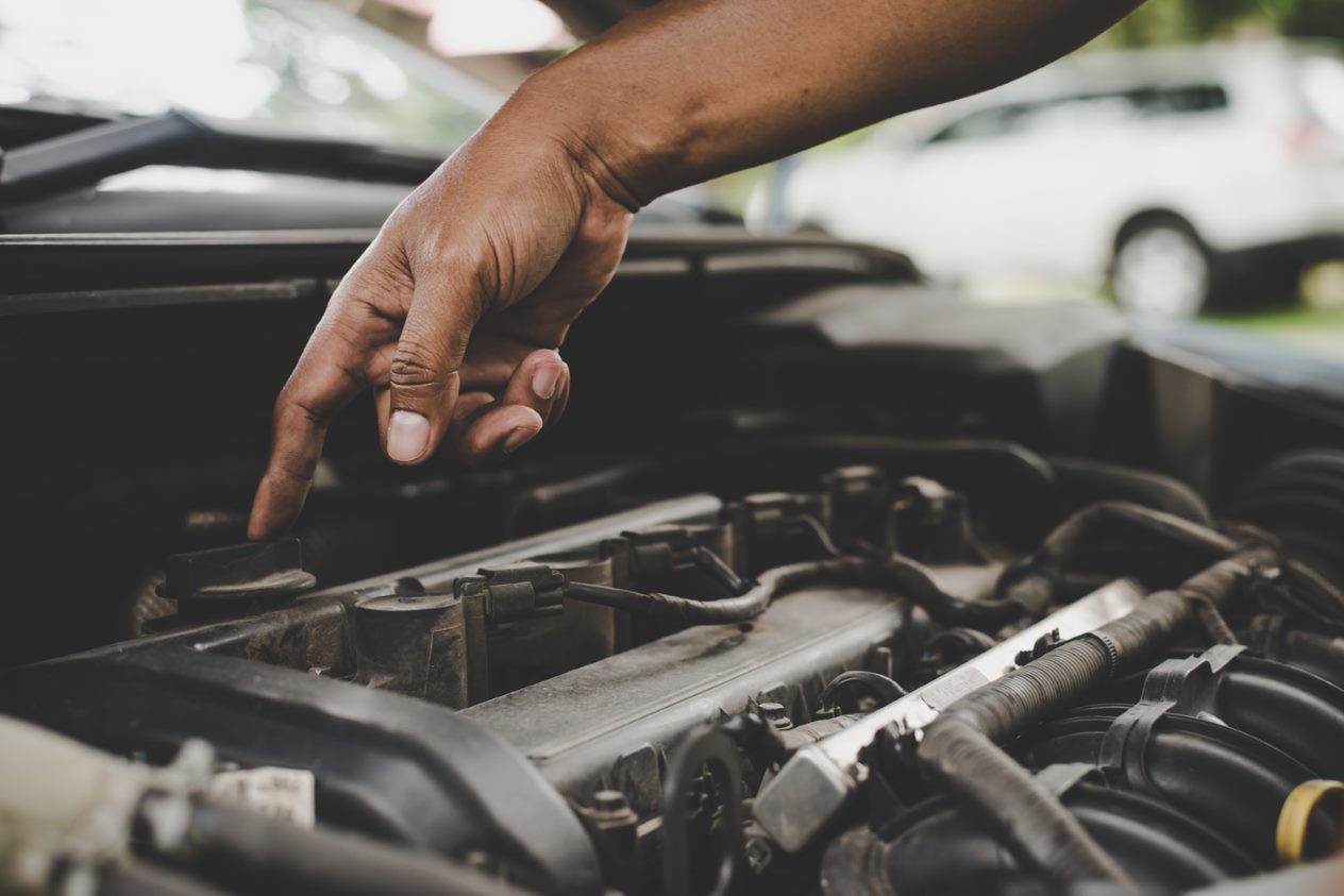 A hand pointing at an engine component under a car hood.