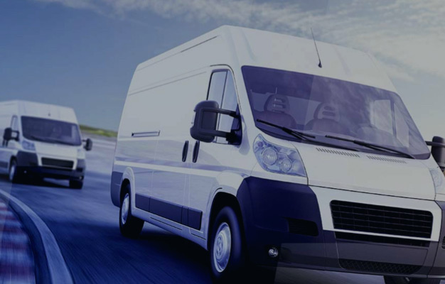 Two white delivery vans driving on a curvy road on a clear day.