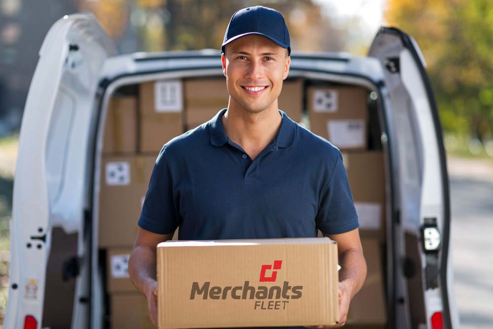 Delivery person holding a Merchants Fleet box in front of an open van filled with packages.
