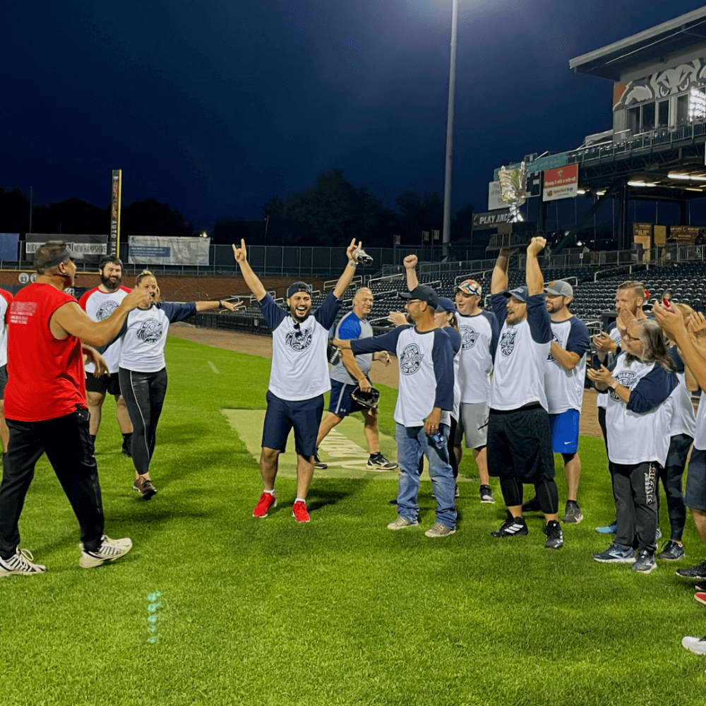 A group of people on a baseball field celebrate a victory, raising their arms in excitement.
